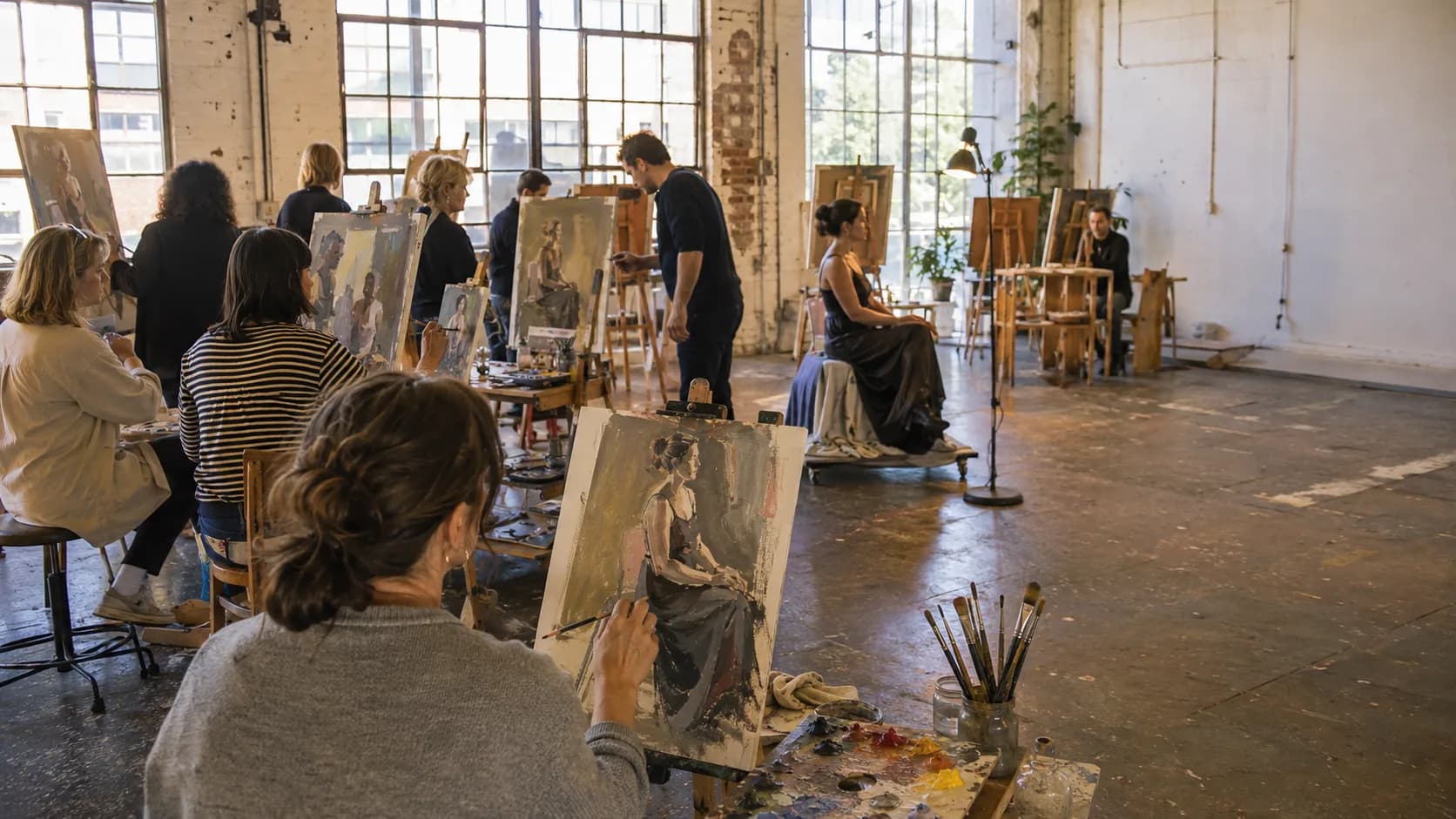Artists work together around tables in a light-filled working studio