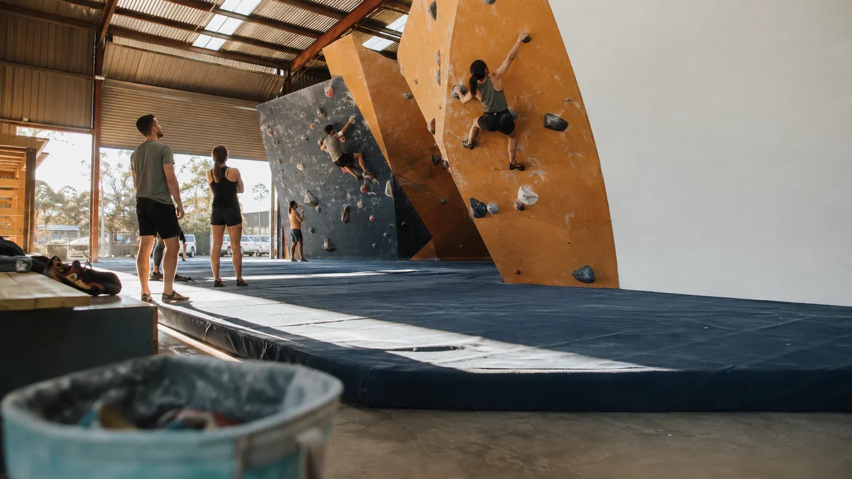 Climbers boulder beneath bright rooflights at an indoor centre in Australia
