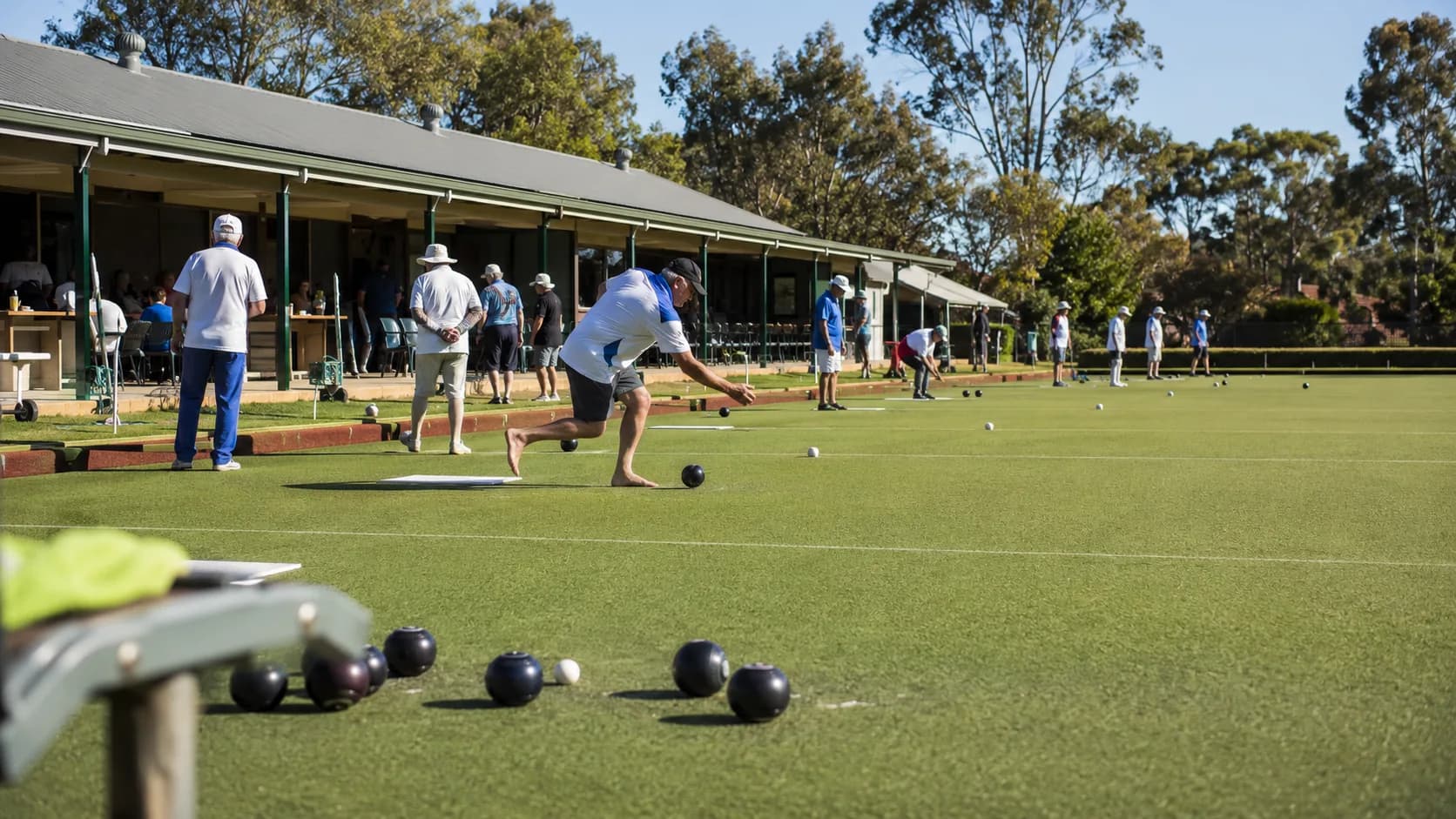 Groups play barefoot bowls across a sunlit club green in Australia