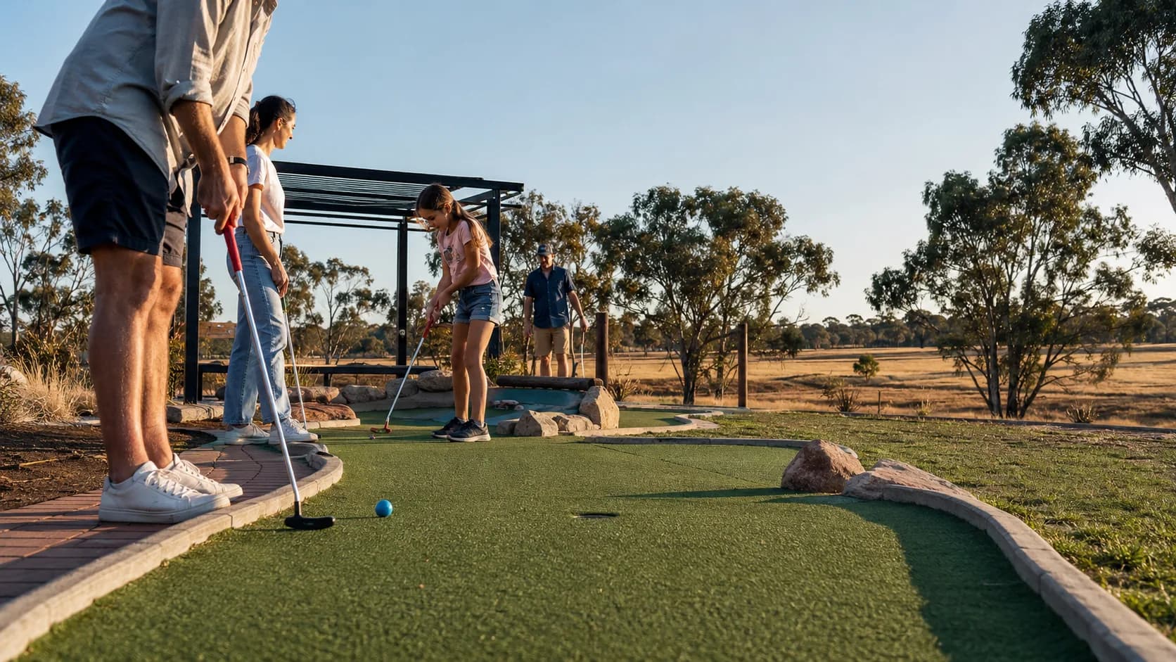 Families play a landscaped mini golf course in an Australian park at dusk