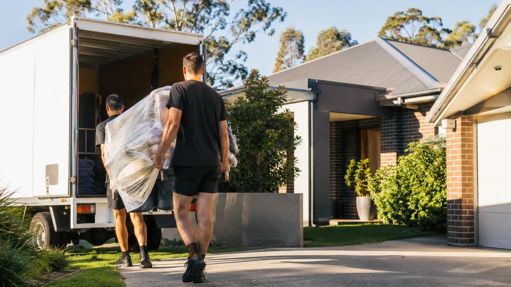 A moving crew carrying a sofa into a truck outside a home in Australia
