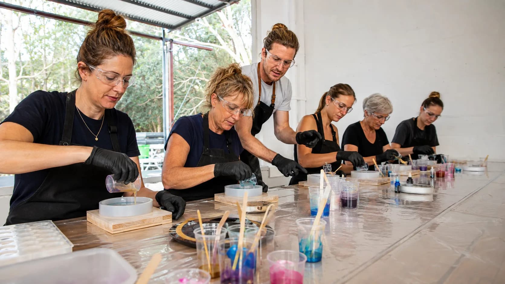 An artist tutor guides a resin pour at ventilated workshop stations in Australia