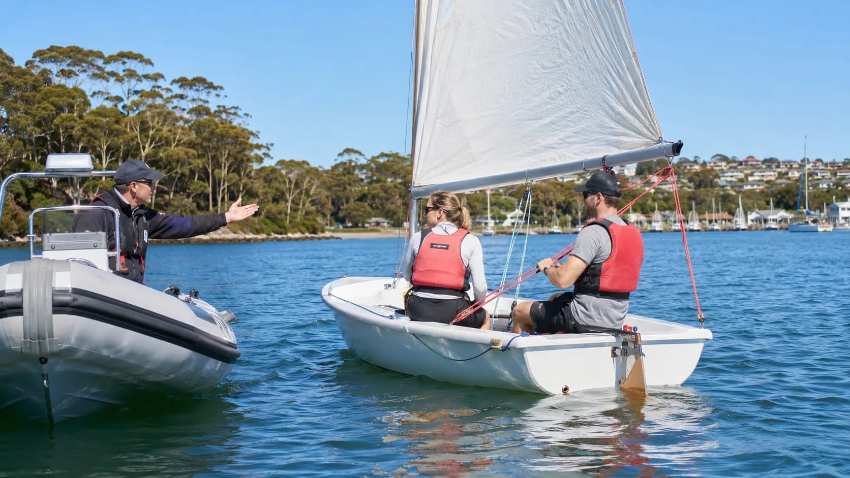 An sailing instructor coaches beginner dinghy sailors on a harbour in Australia
