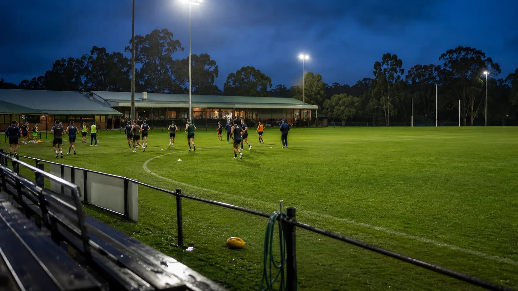 Community teams train across a marked sports oval at sunset in Australia