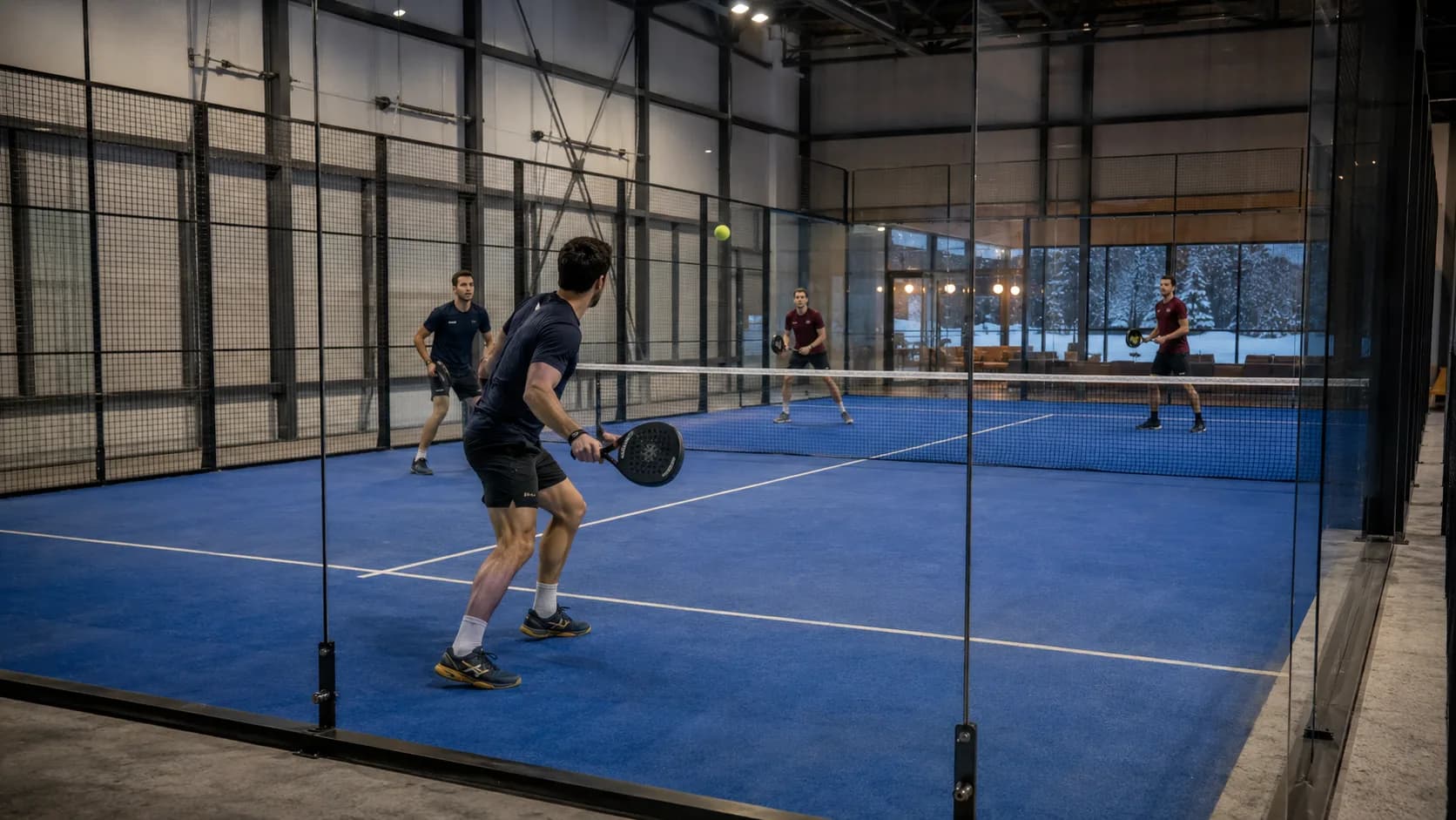 A glass-walled indoor padel court at a Canadian facility, lit and ready for evening doubles