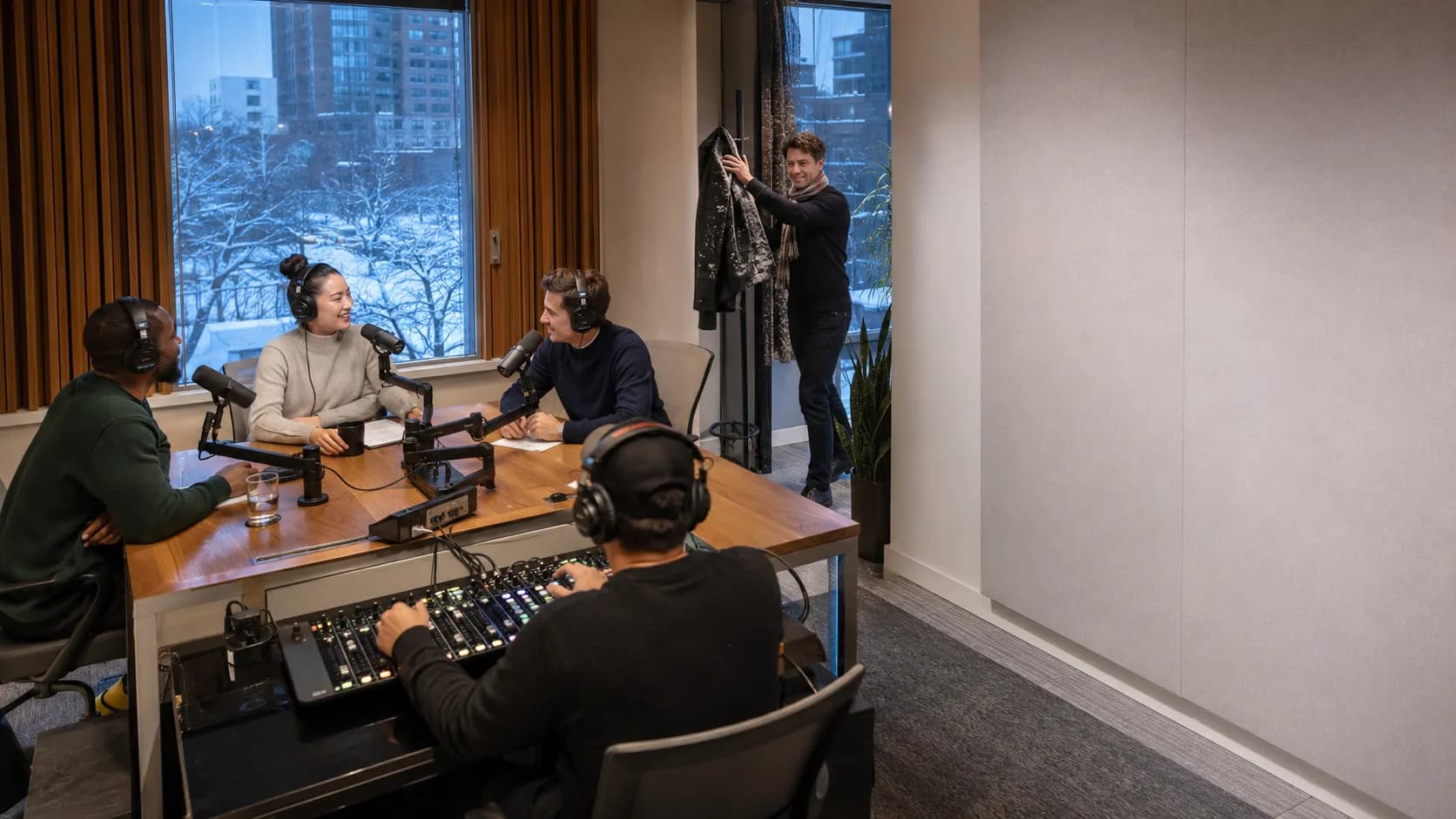 Two hosts record a podcast inside a warm Canadian studio in winter