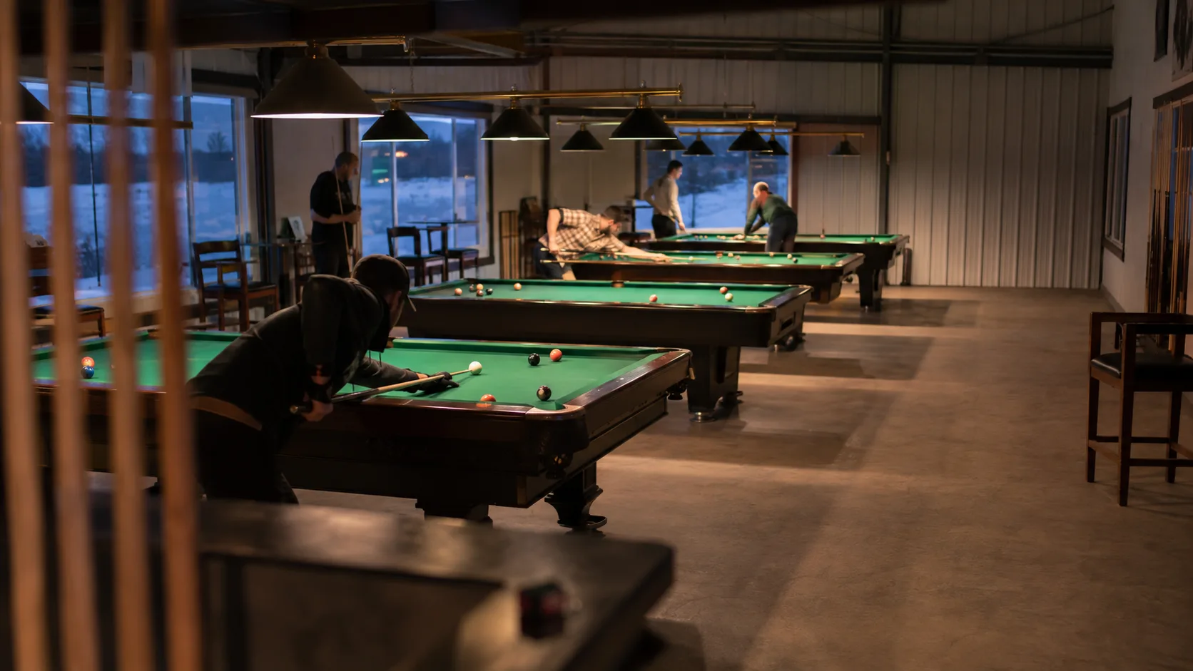 Players gather around pool tables inside a warm Canadian winter venue