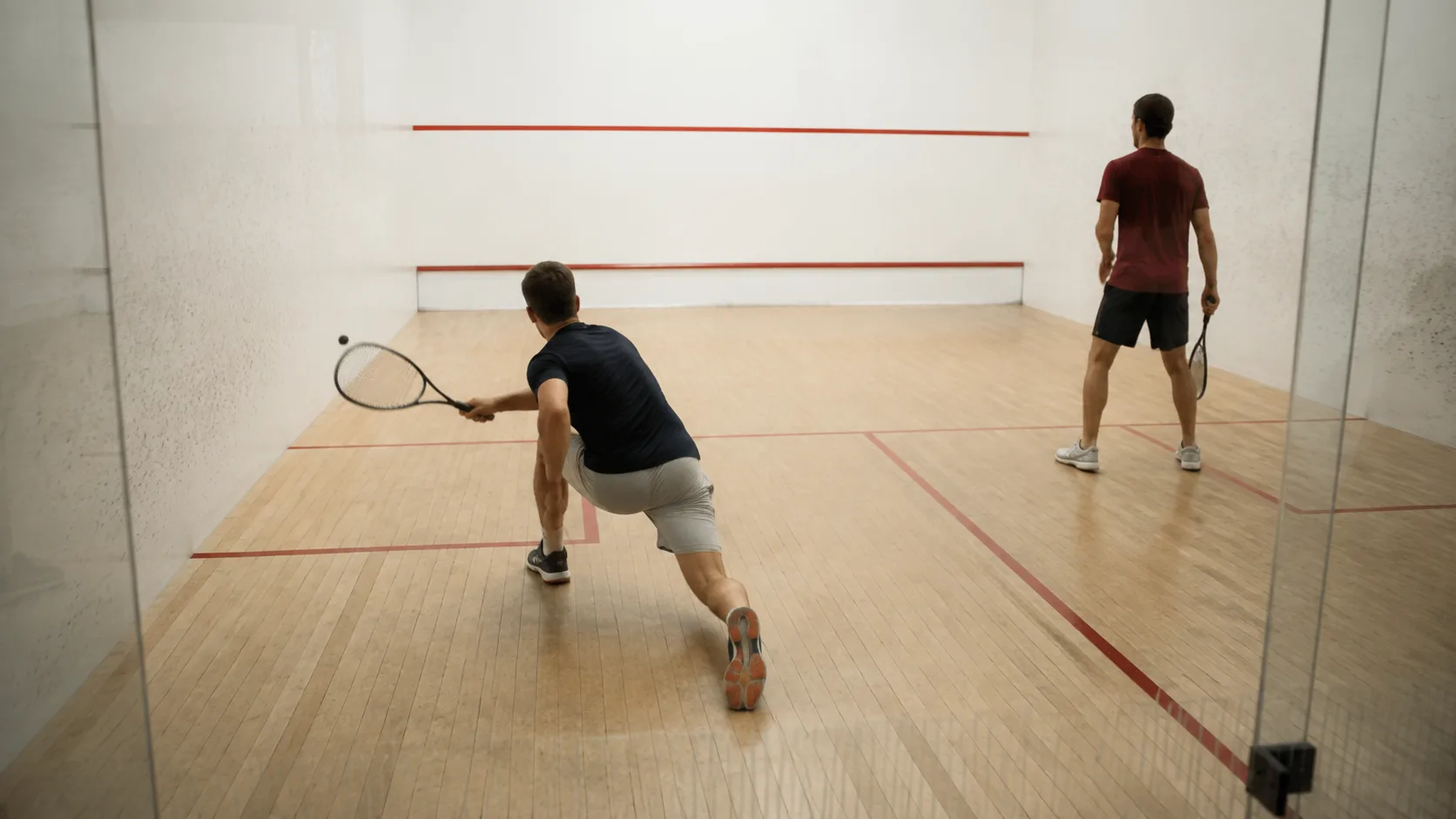 A squash court at a Canadian club, glass-backed and lit for evening winter play