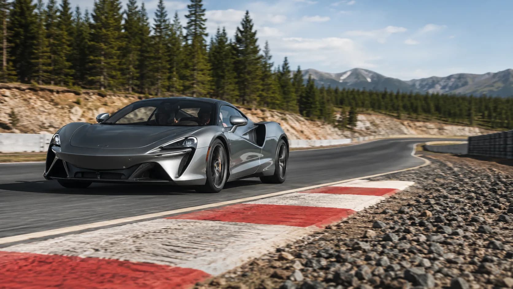 An exotic car waits in a Canadian road course pit lane with pines behind it