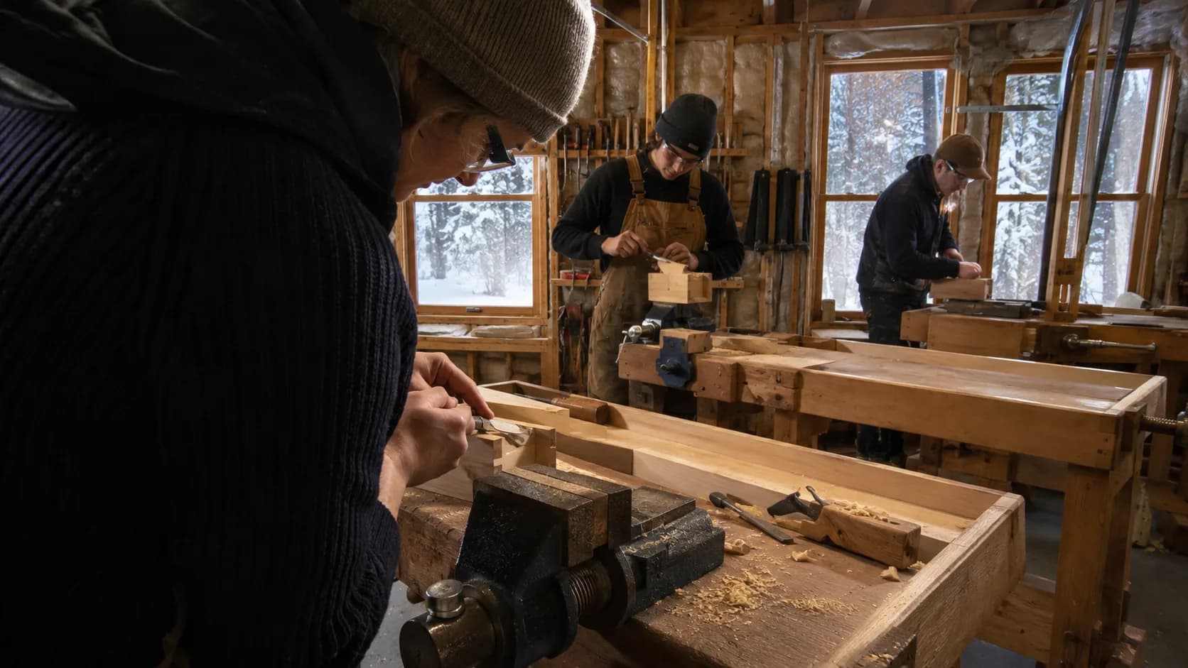 A woodworking instructor and two students at vice-fitted benches in a bright timber shop in Canada