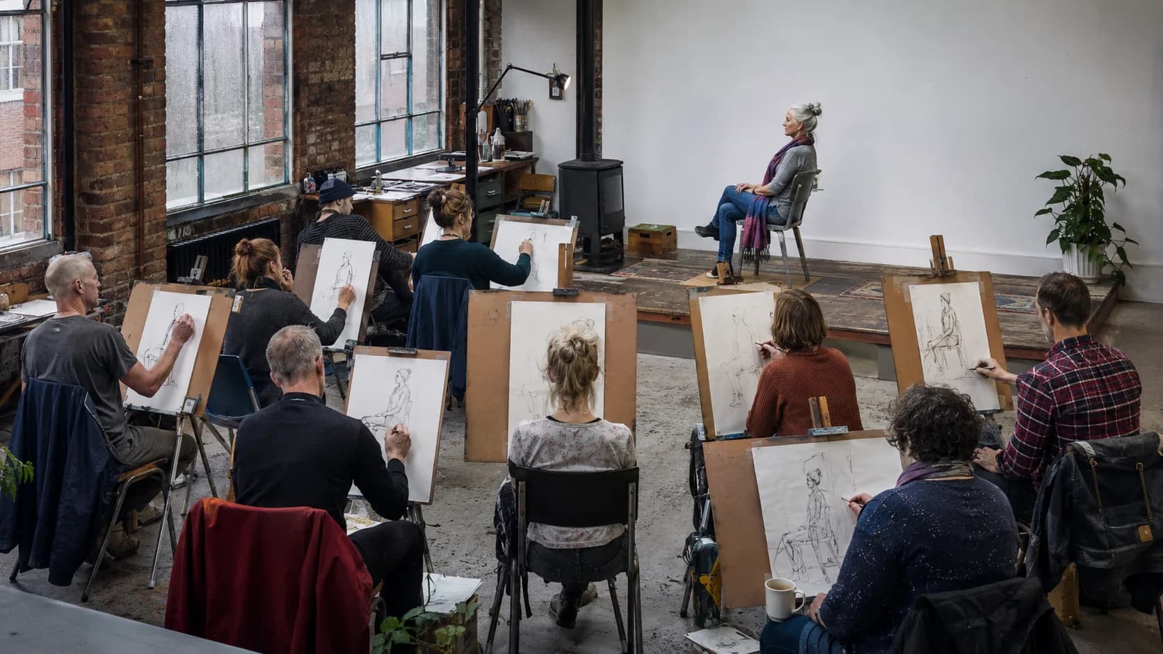 Artists work together around tables in a light-filled working studio