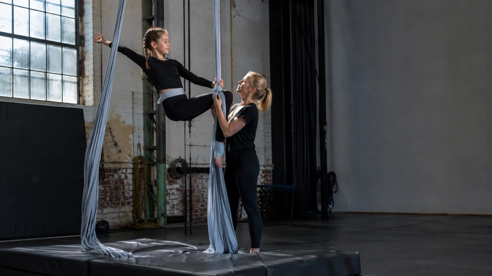Aerial coach guiding a student on silks at a circus school in the UK