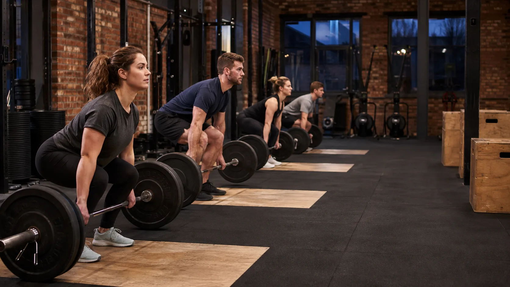 Athletes on rowers and racks inside a brick railway arch gym in the UK at dusk