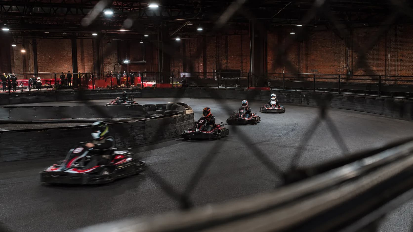 Drivers race beneath bright lights at an indoor circuit in the UK