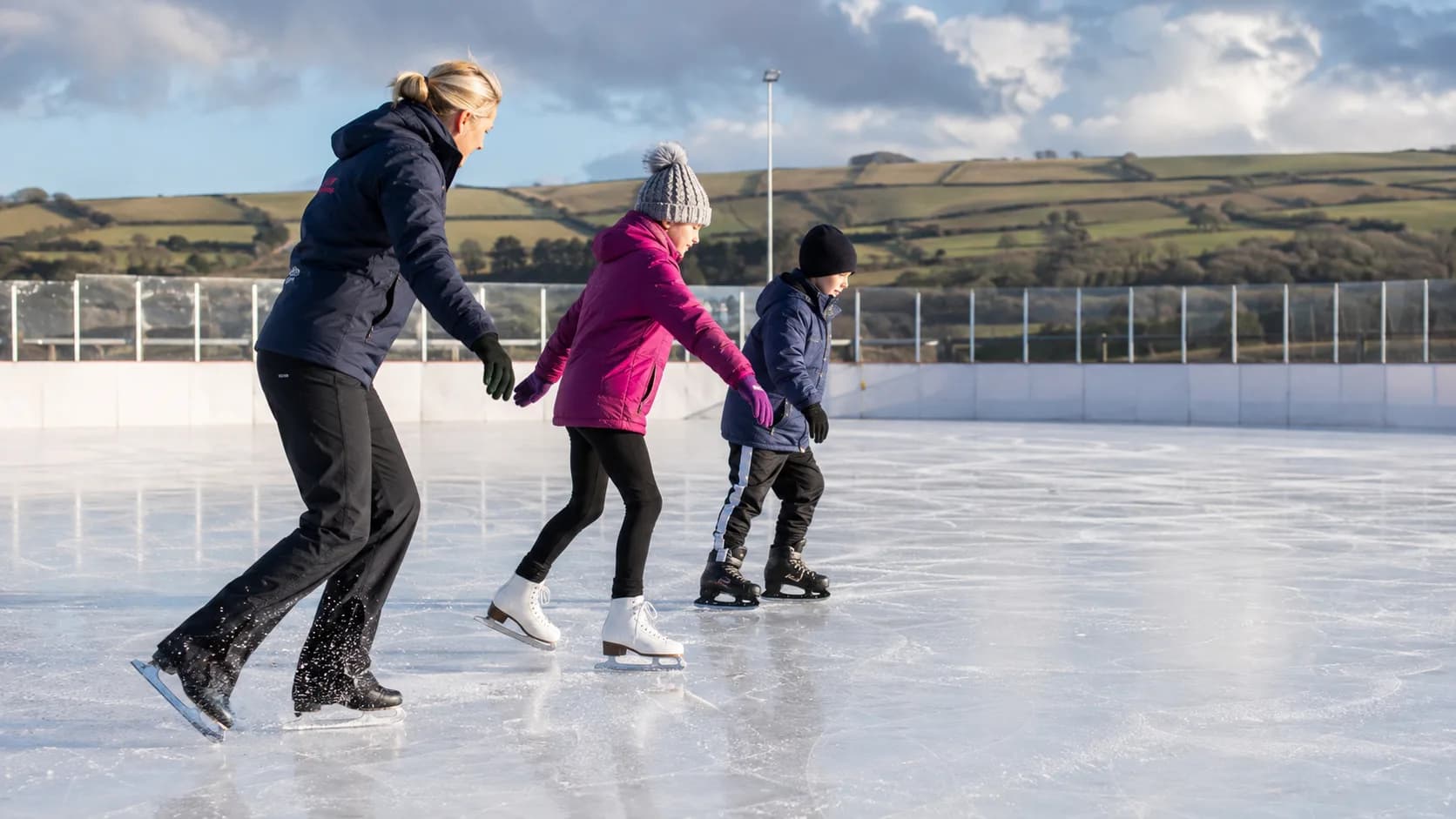 Skaters circle a busy indoor rink at a UK leisure centre under bright lights
