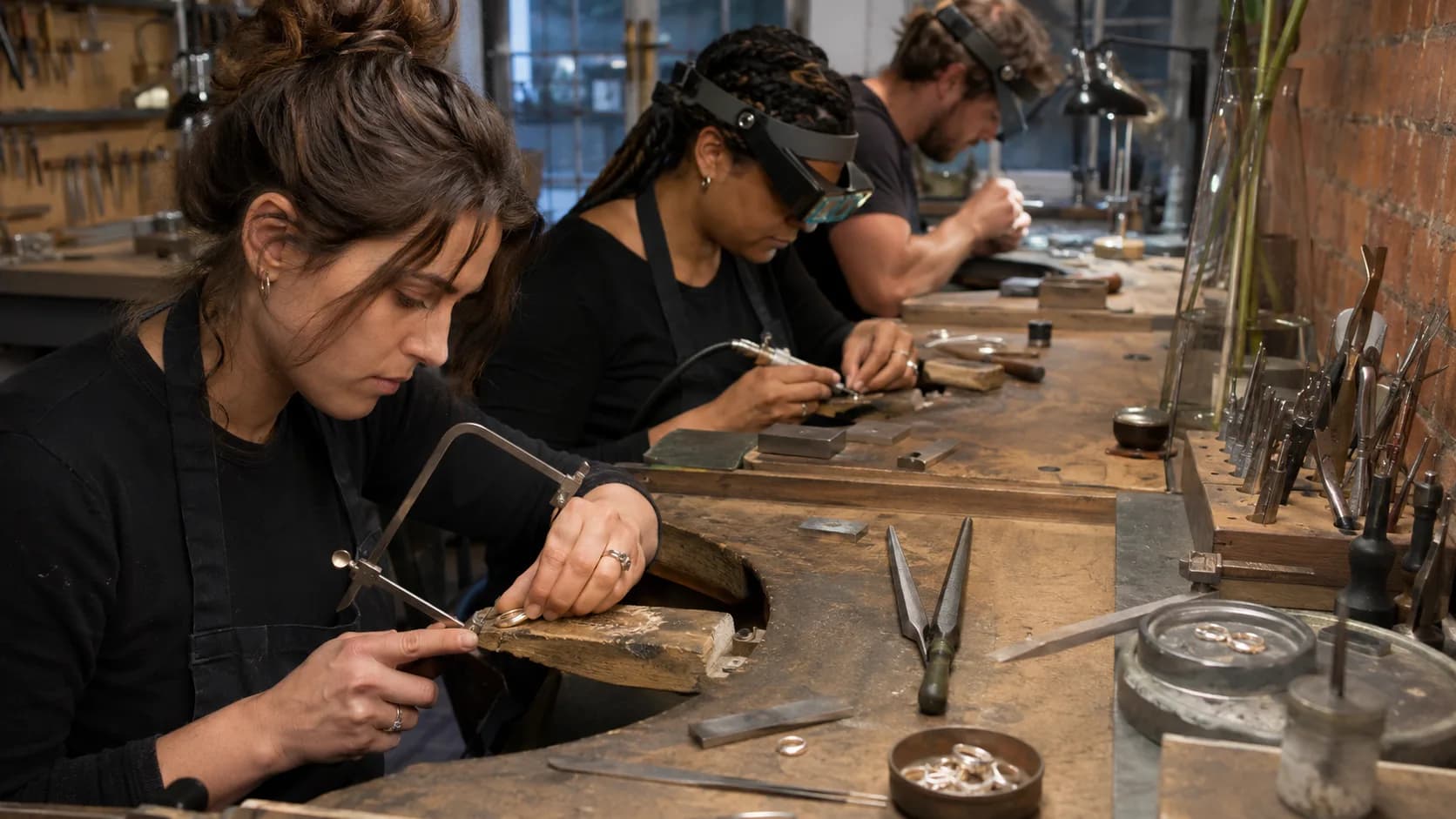 A tutor and two makers at separate benches soldering silver in a UK jewellery workshop
