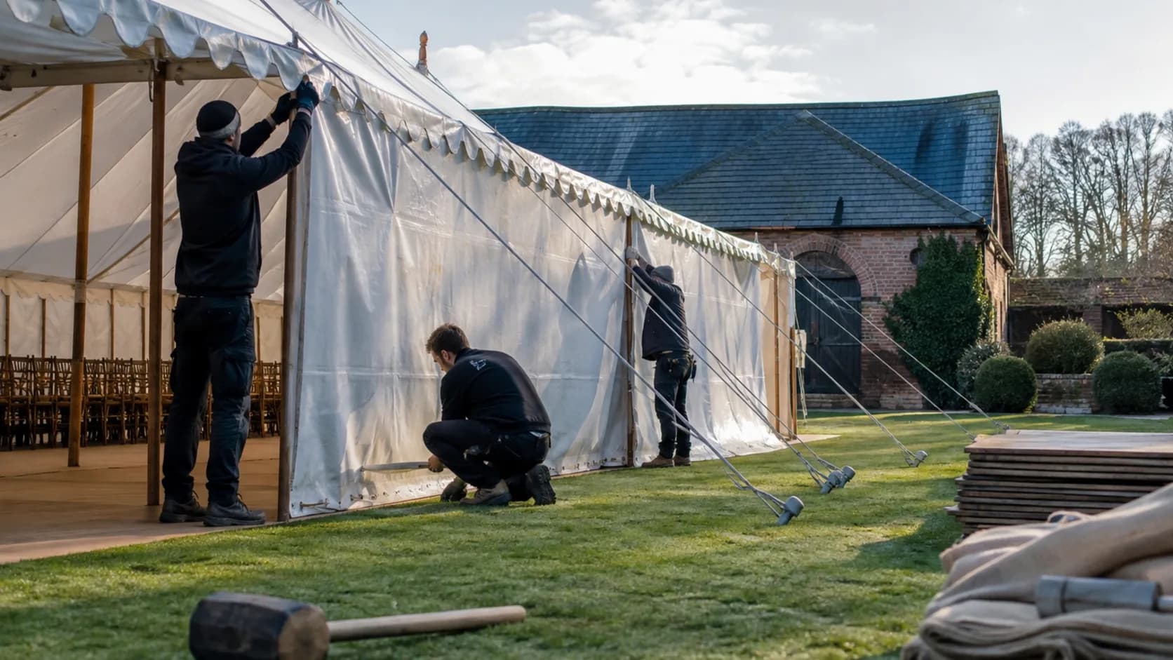 Crew tensioning a marquee wall beside a country venue in the UK