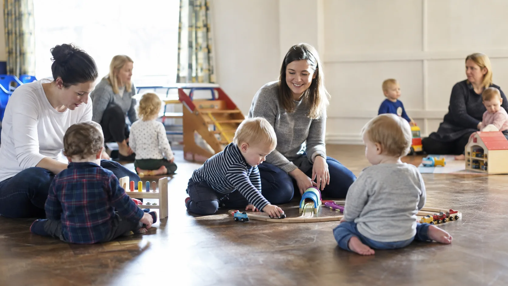 Toddlers and carers at an active playgroup in a hall in the UK