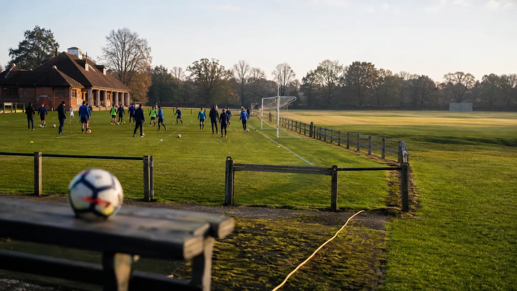Club teams train on striped grounds beside a brick pavilion in the UK