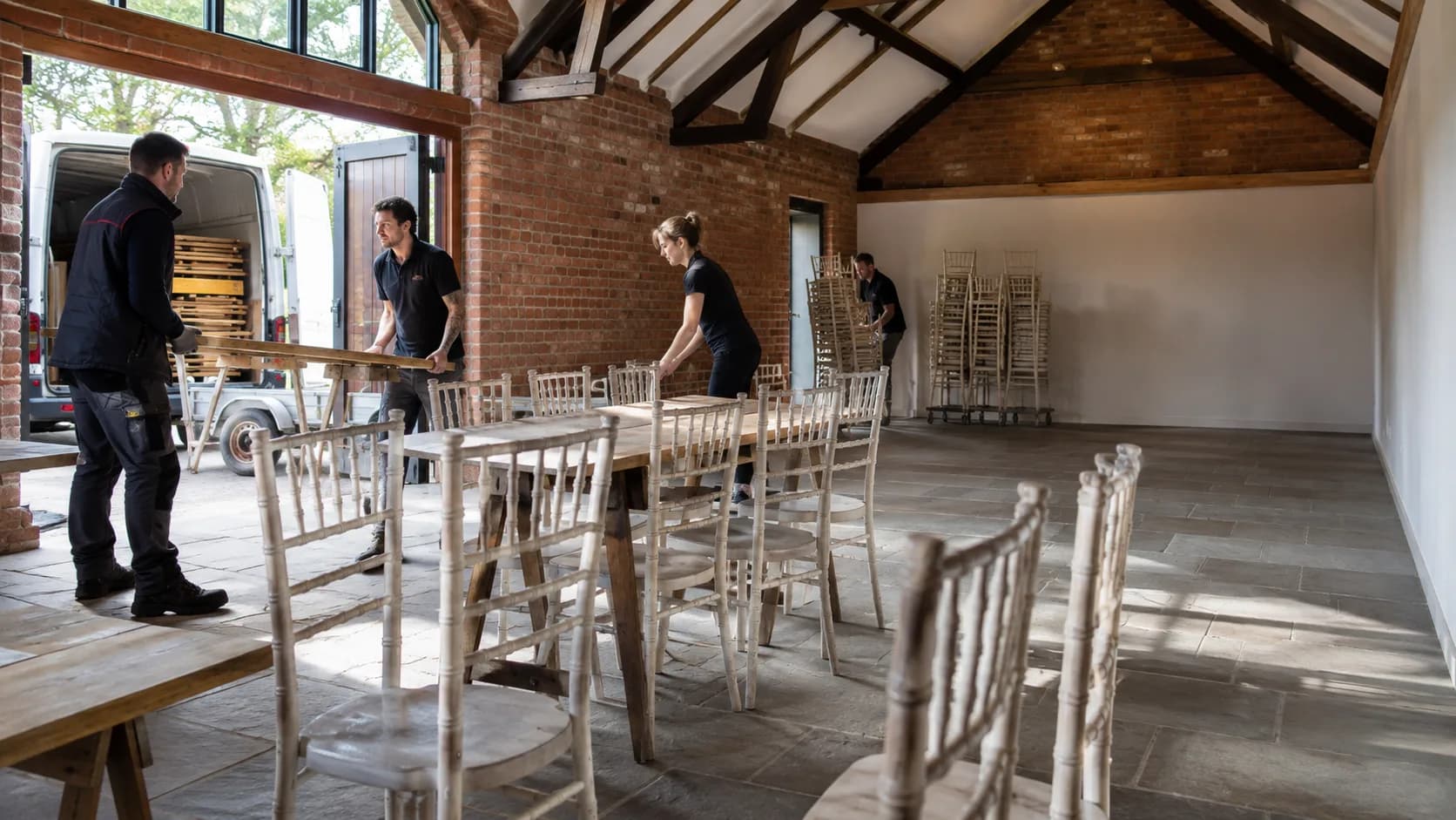 Crew arranging chairs and tables inside a barn venue in the UK