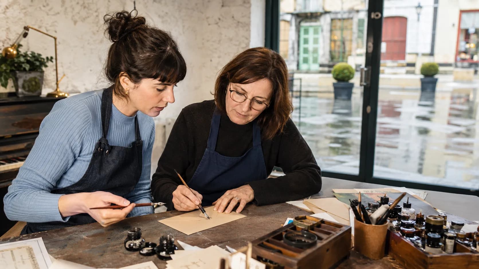 A tutor demonstrates uncial letterforms with a broad-edged pen at a parish hall table in Ireland