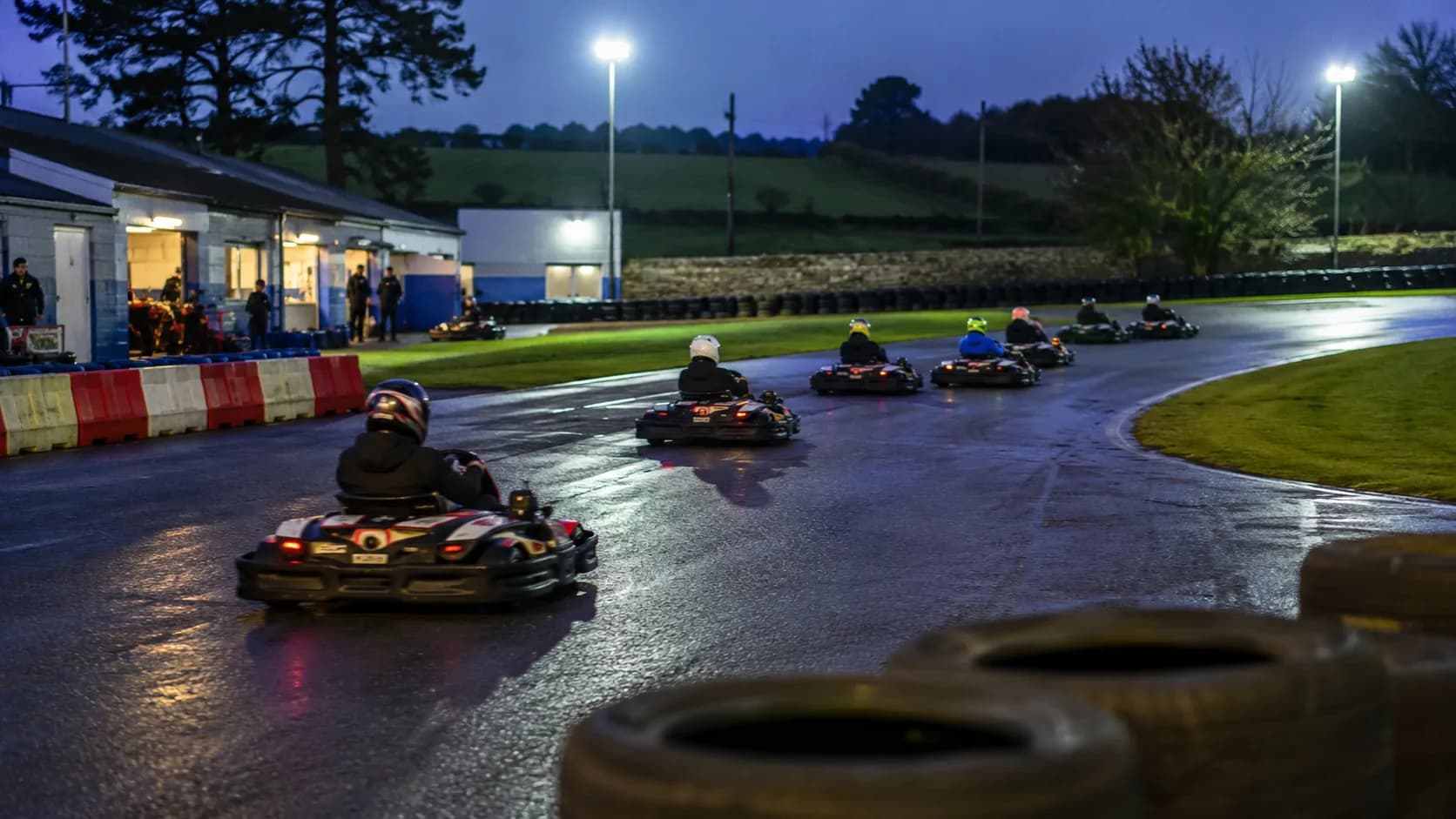 Groups race go-karts around a floodlit outdoor track in Ireland