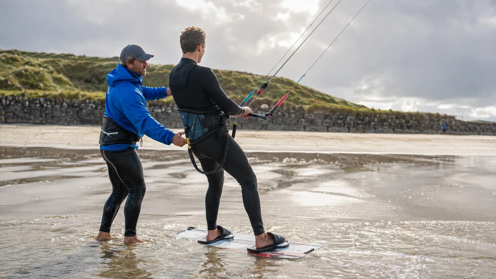 A learner practises board starts with an kitesurf instructor on a strand in Ireland