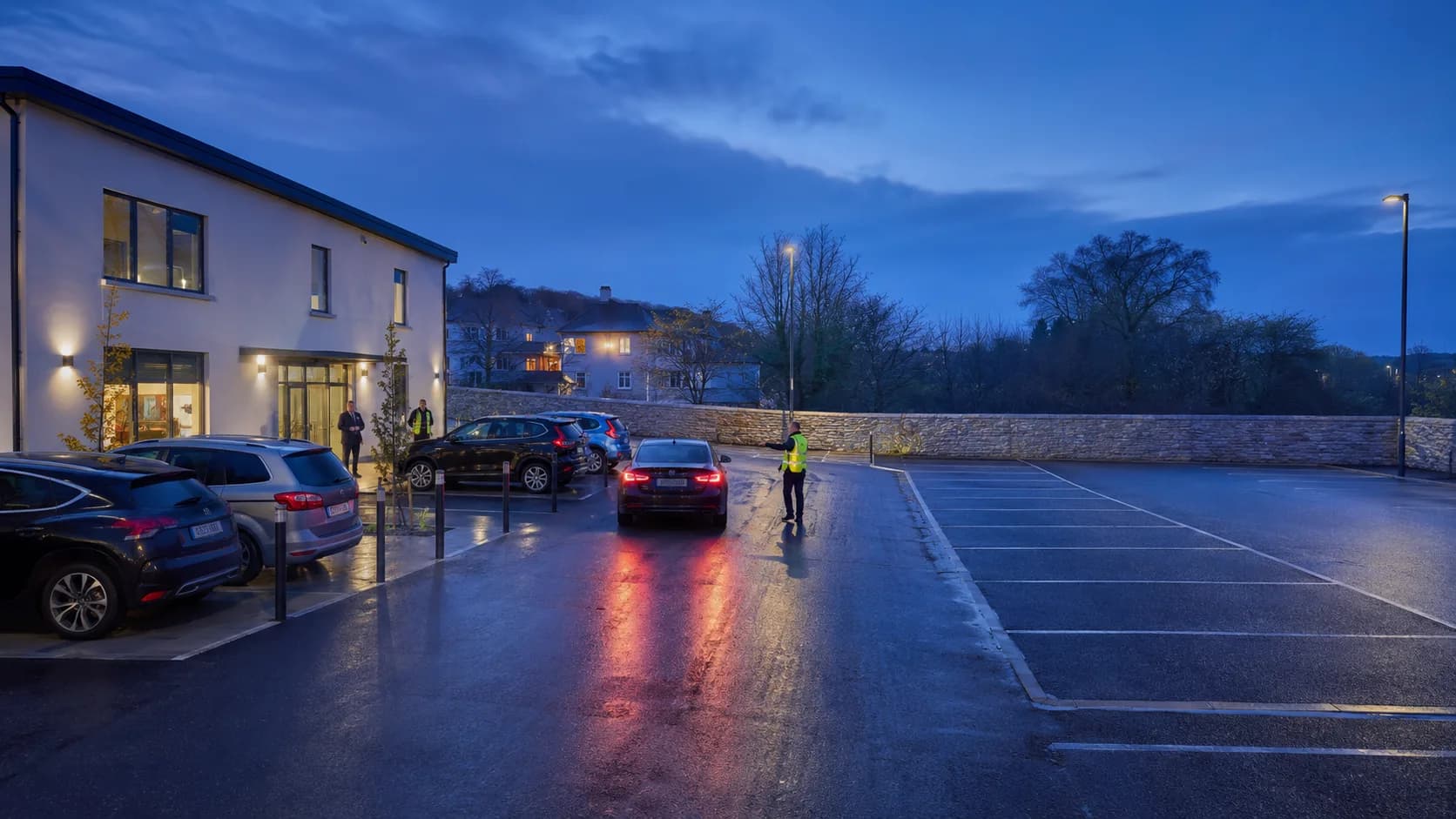 Visitors arrive beside a rendered urban car park at dusk