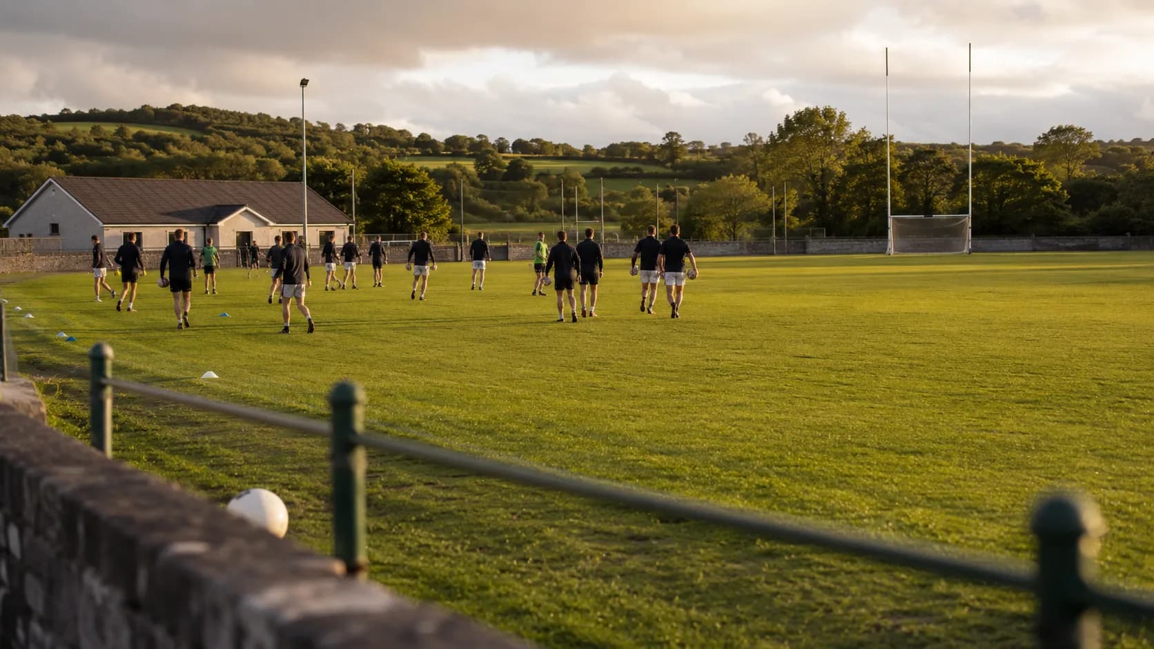 Players practise across a green community pitch at an Irish sports ground