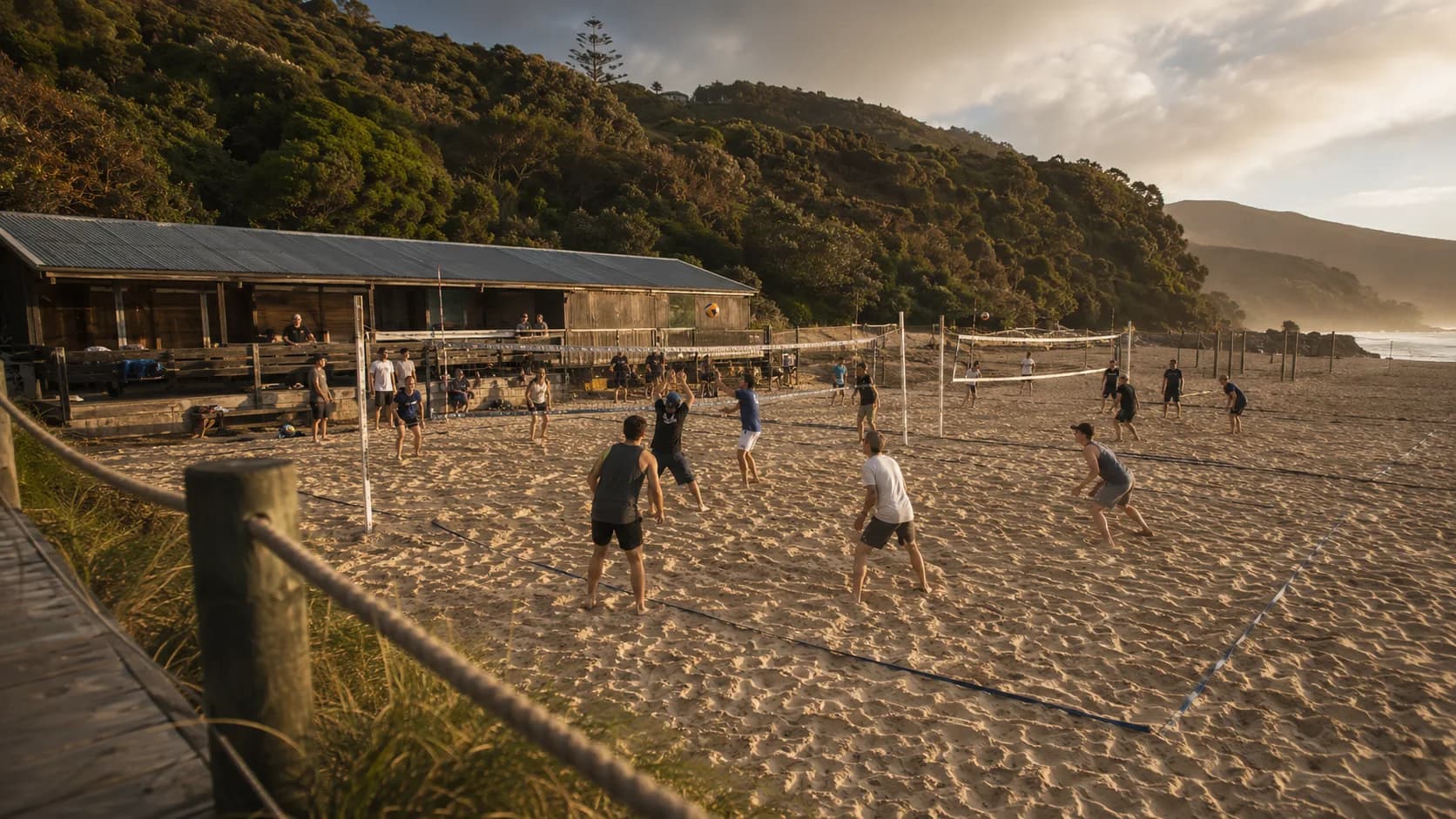 Groups play beach volleyball beside green coastal hills in New Zealand