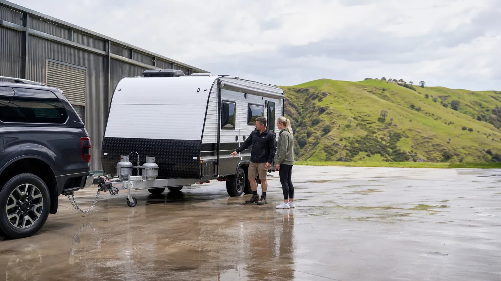 Travellers inspecting a caravan hitch after rain in New Zealand