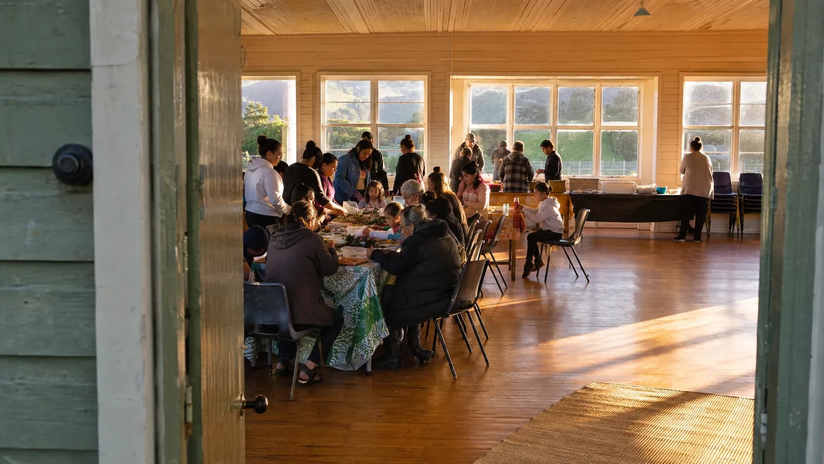 A community workshop fills a timber hall beneath green hills