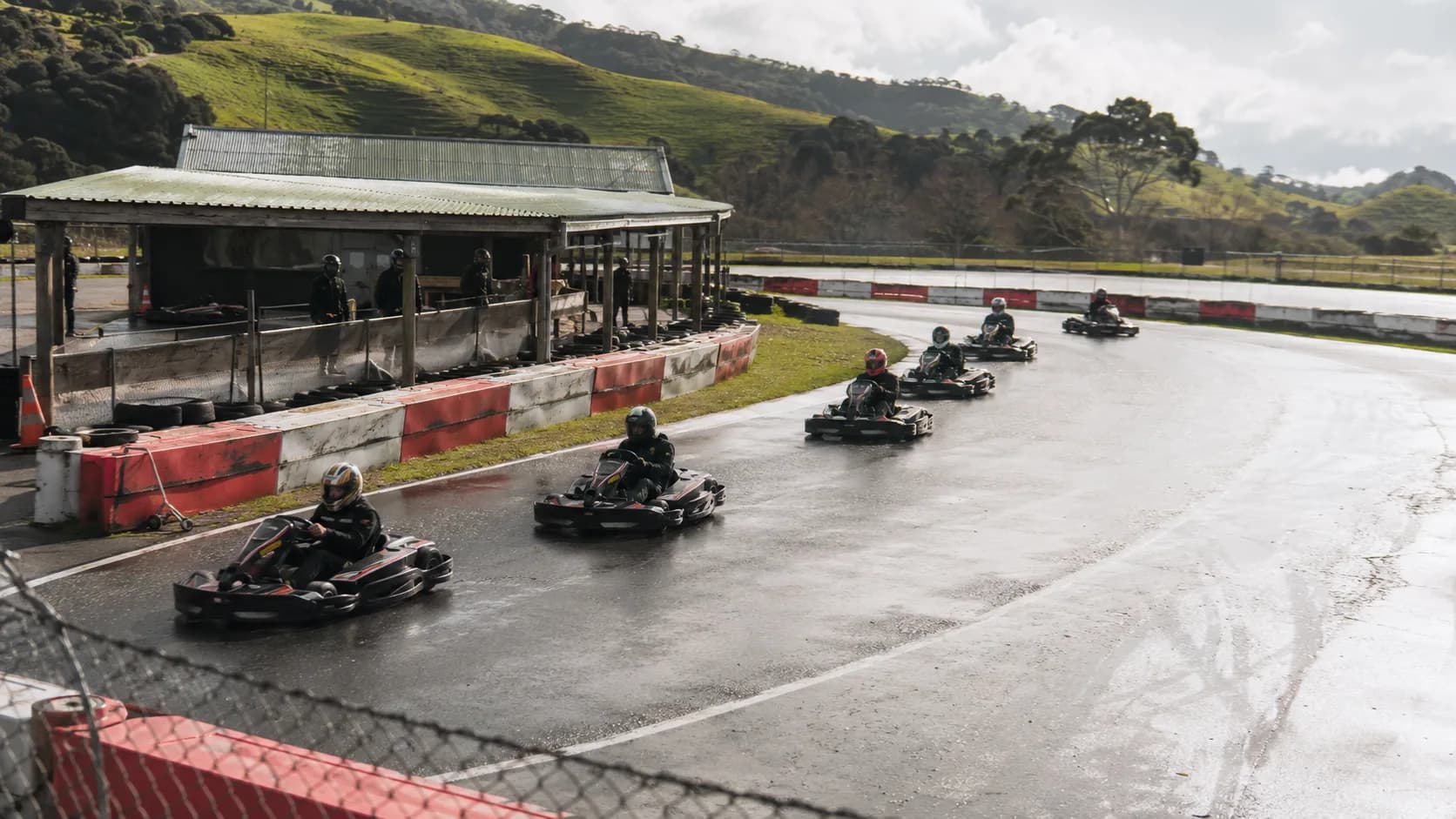 Karts round a damp circuit beside green hills in New Zealand