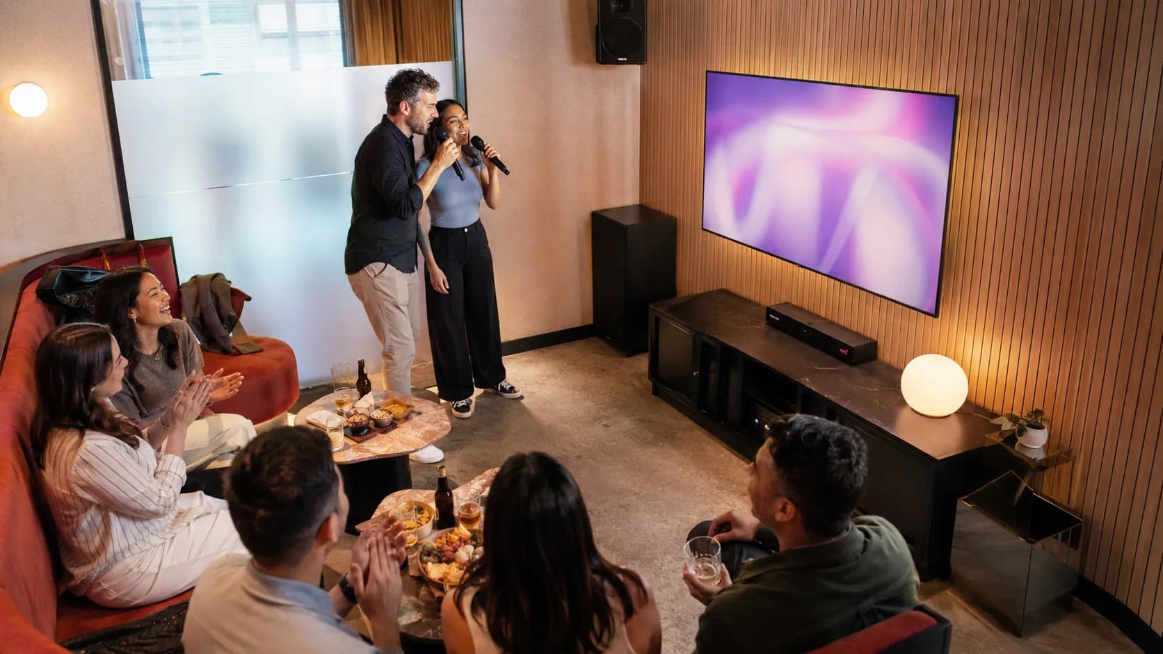 A group shares microphones in a warm timber-lined karaoke booth