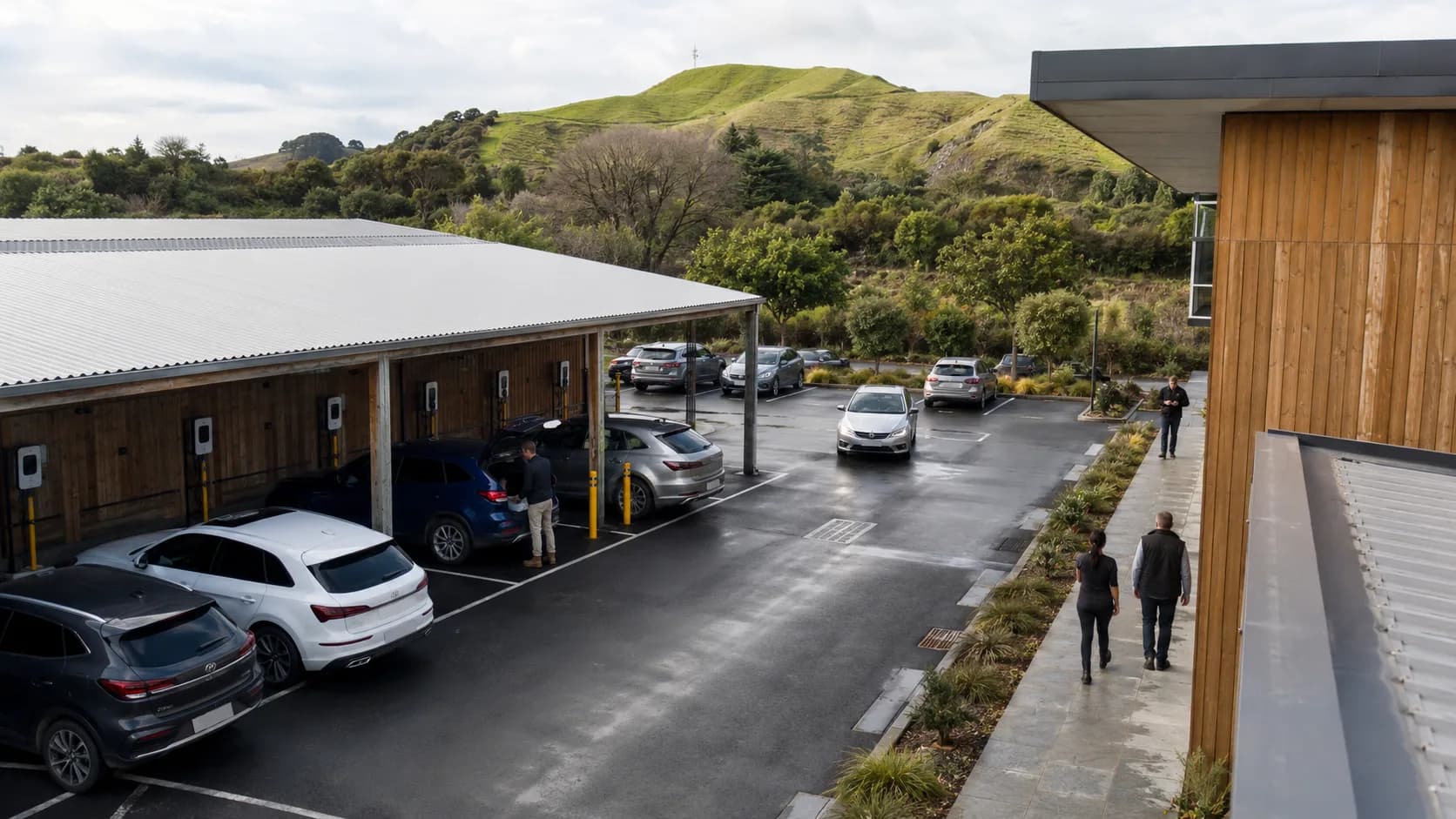 Cars occupy a wet timber-edged workplace car park below green hills