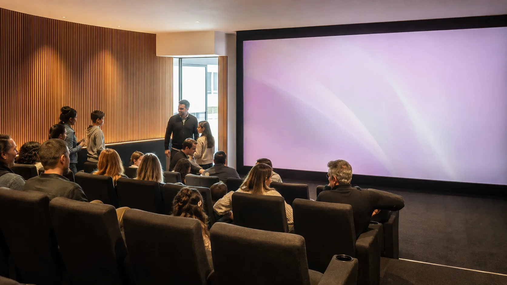 A small audience watches a bright private cinema beneath timber acoustic panels