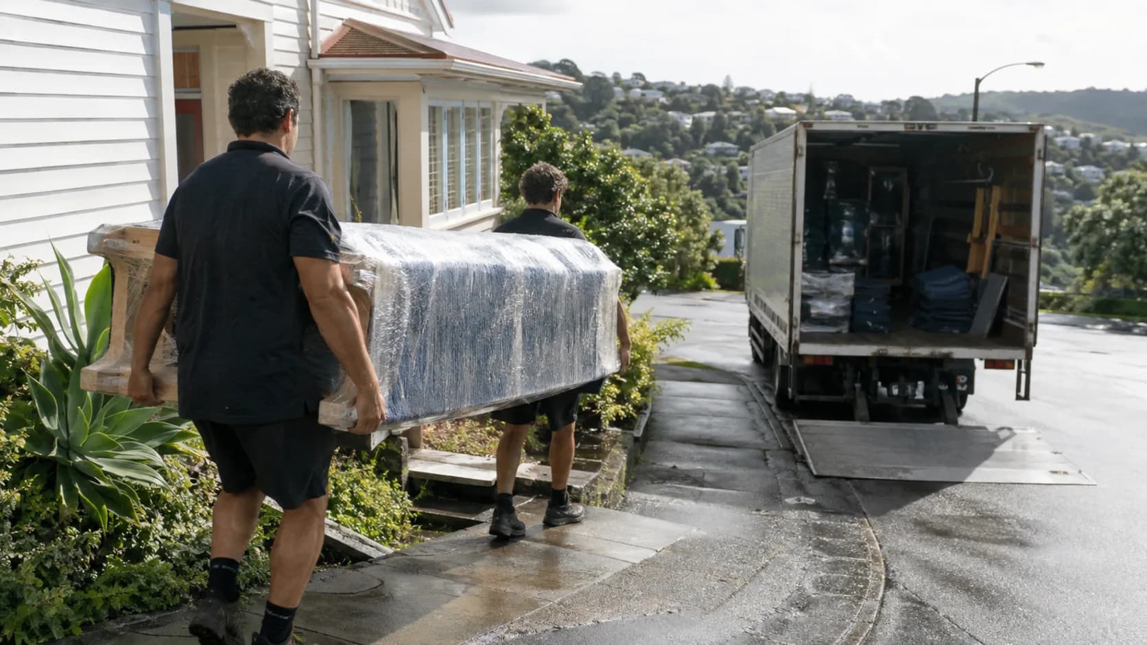 A moving crew carrying a sofa into a truck outside a home in New Zealand