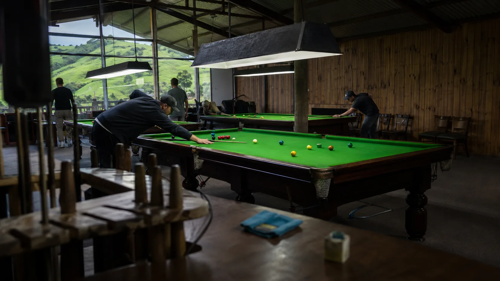 Friends play pool beside a timber club interior in New Zealand