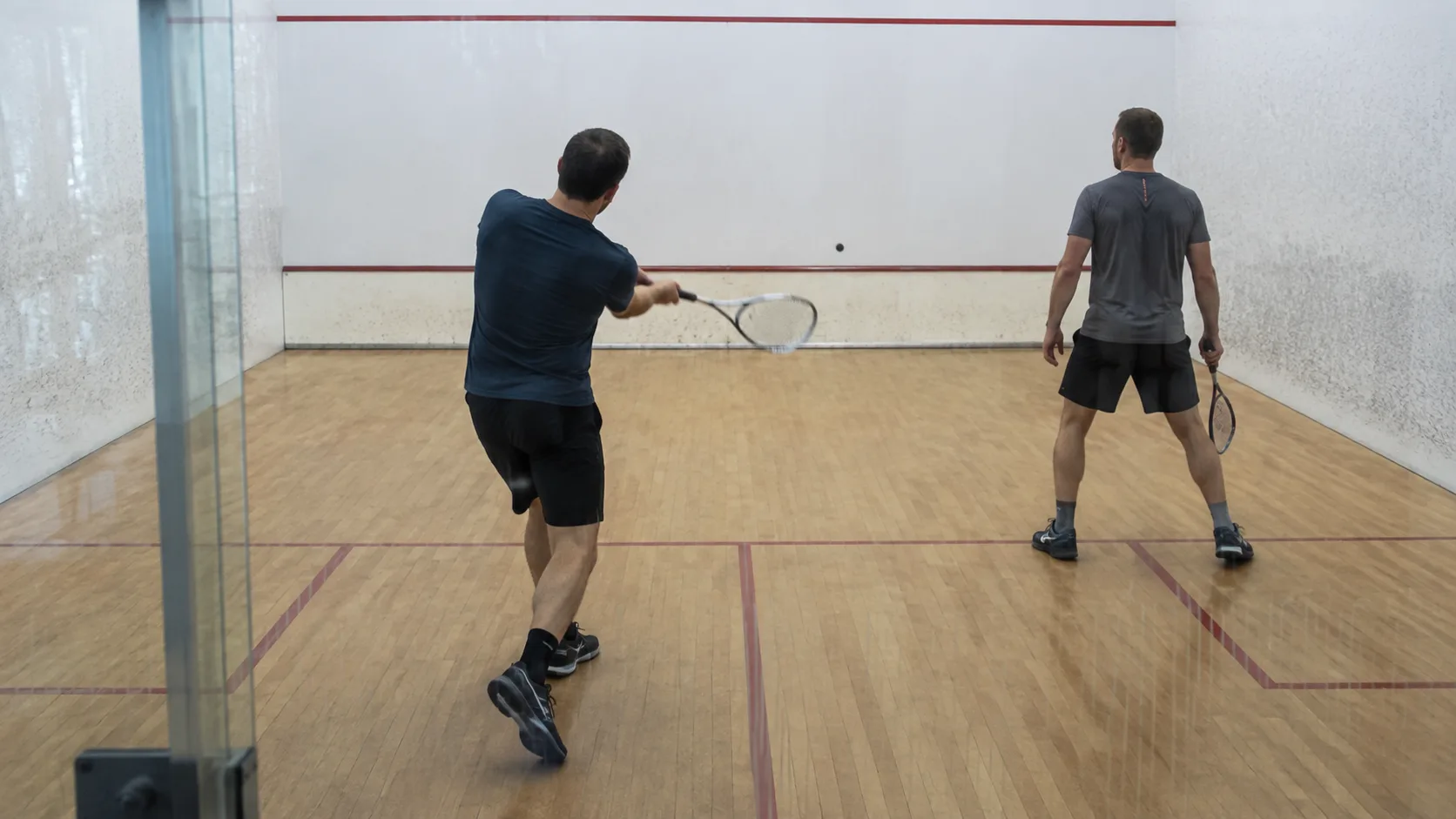 A squash court at a New Zealand club, glass-backed and lit for evening play