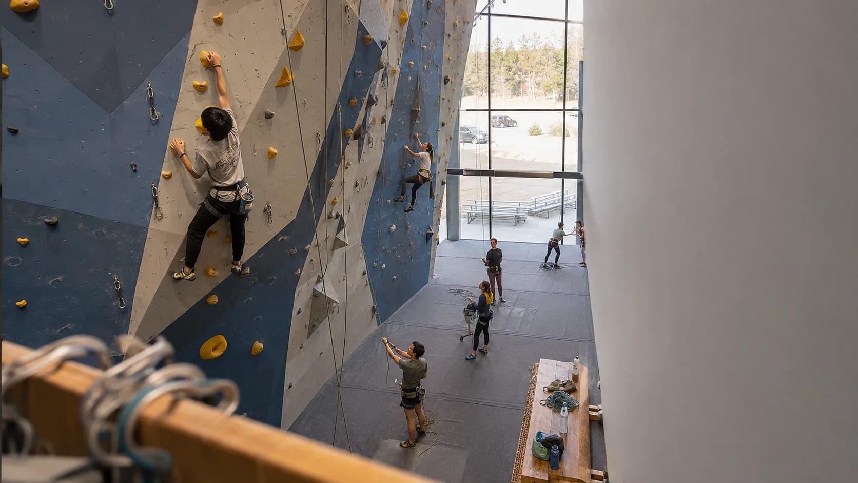 Climbers cross tall routes inside a busy modern gym in the US