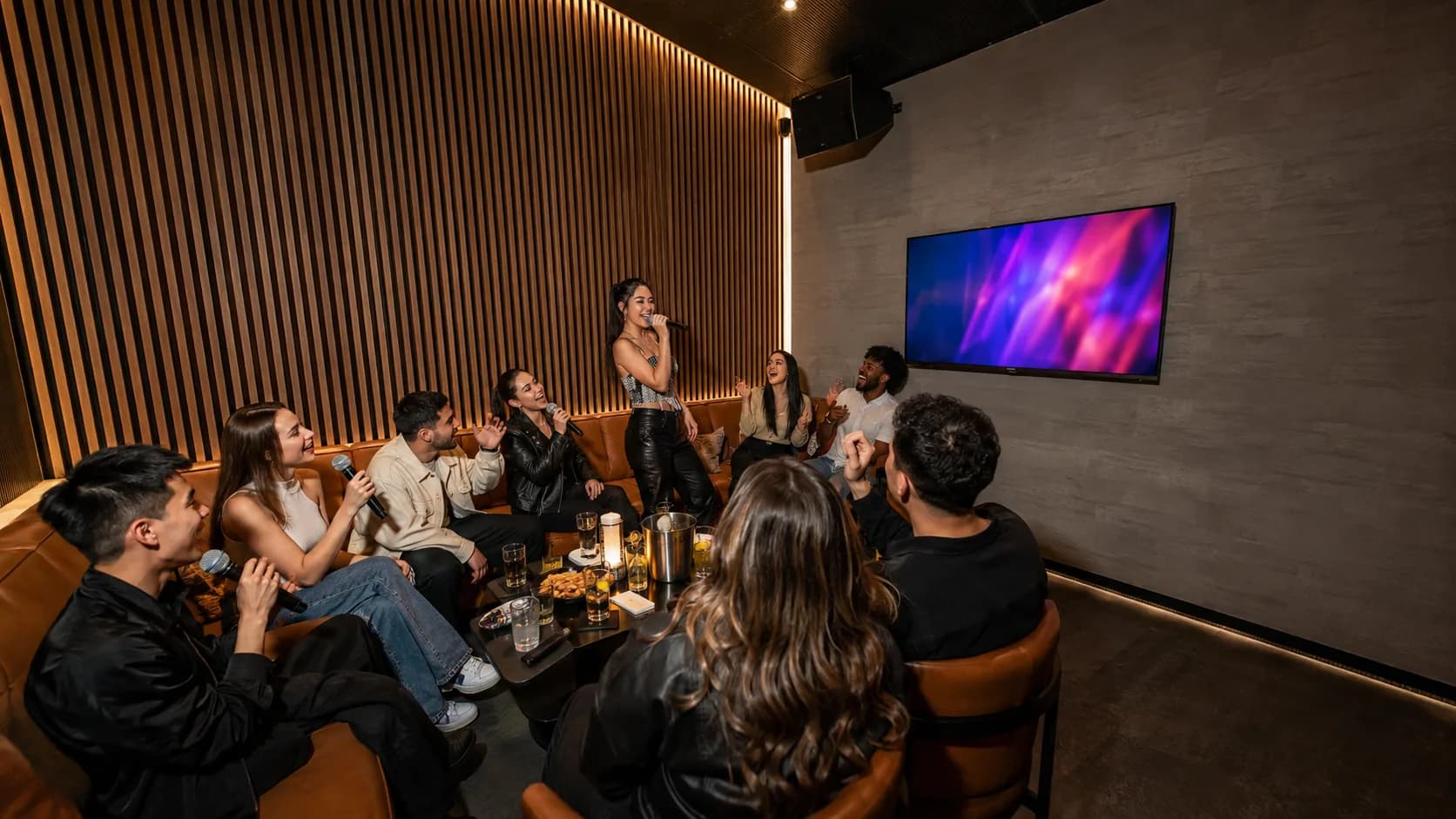 Friends perform together in a polished private karaoke suite at night