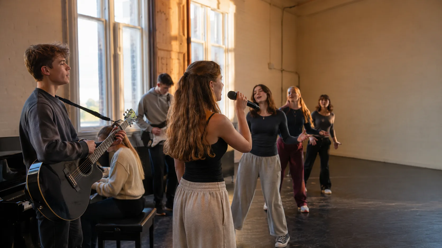 Musical theater instructor coaching a lively ensemble in a studio in the US