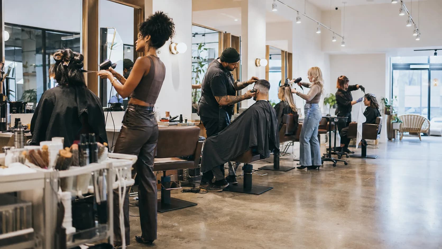 Independent stylists work from occupied chairs inside a bright shared salon