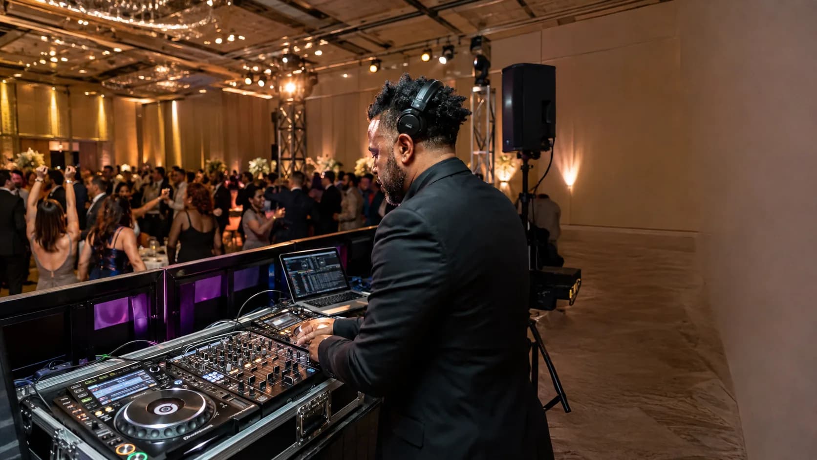 Professional DJ mixing beside a busy wedding dance floor in the US
